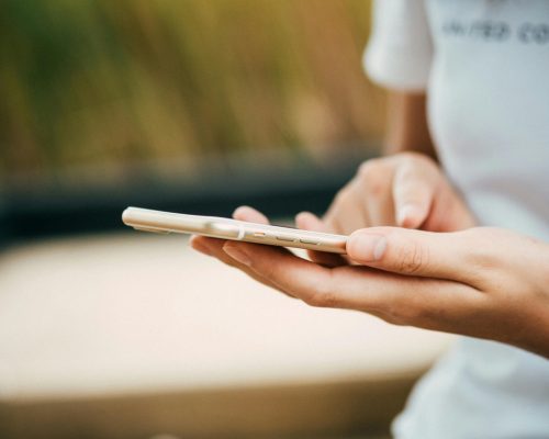 Close-up of a person using a smartphone outdoors, focusing on hands and device.